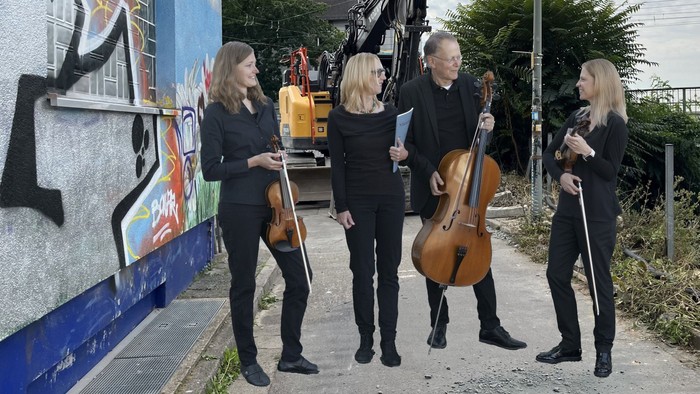Vier Musiker mit Streichinstrumenten posieren vor Graffiti-Wand