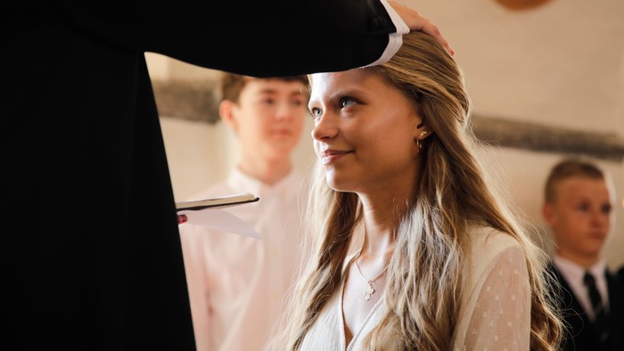 En ung pige med lang blond hår og hvidt top, ser opad og smiler.