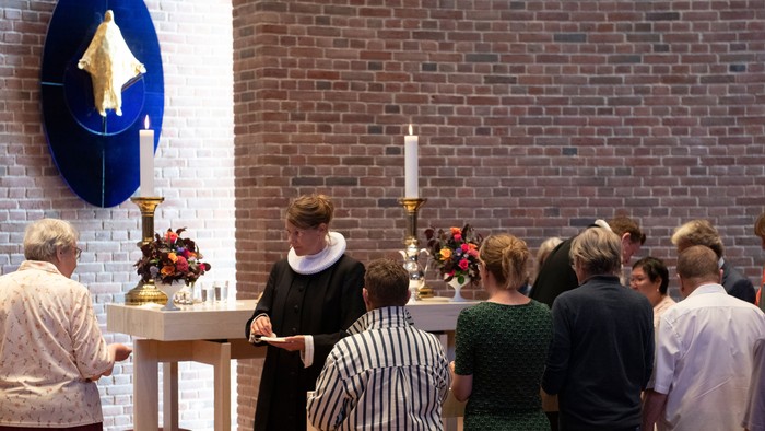 En præst ved alteret i en kirke med en gruppe mennesker.