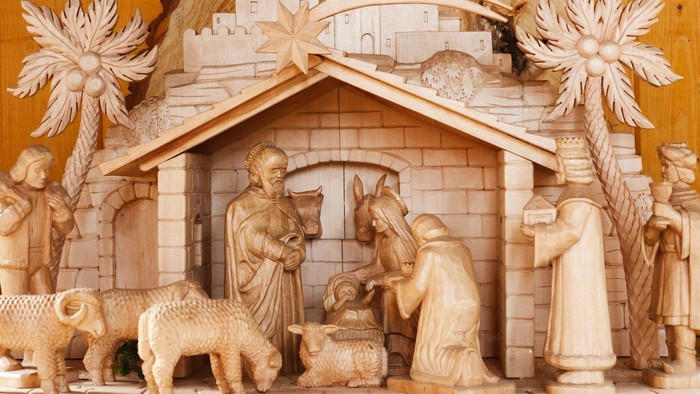 Die Holzskulptur zeigt eine Krippe mit Maria, Josef, dem Baby Jesus, einem Esel und einer Kuh.
