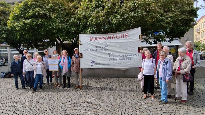 Auf dem Marktplatz stehen die Mitglieder der Mahnwache und halten ein Transparent hoch.