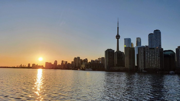 City skyline at sunset with a large tower and water in the foreground
