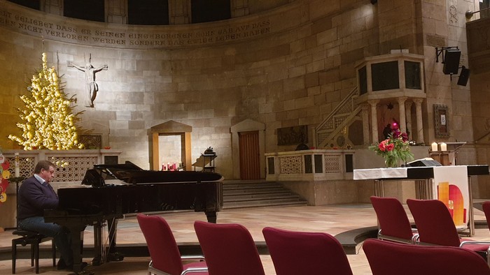 Ein Mann spielt Klavier in einer Kirche, geschmückt mit Weihnachtsdekorationen.