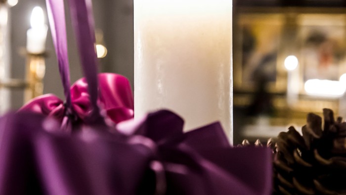Elegant lys dekoreret med lilla bånd og omgivet af festlig grønt og kogler.