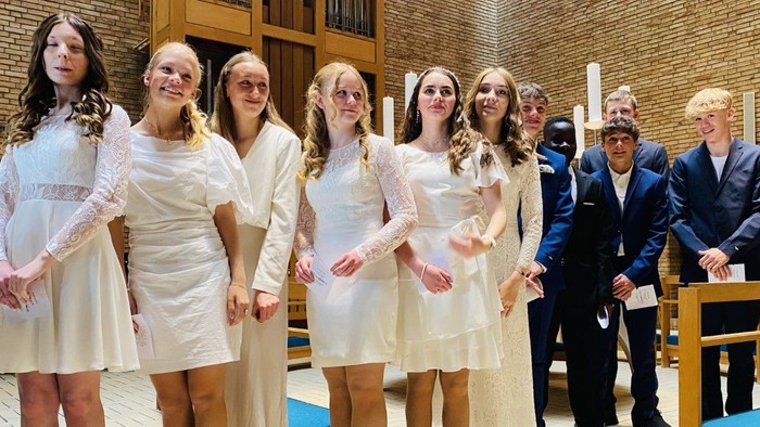 En gruppe unge piger i hvide tøjer og mænd i formelle klæder står sammen i en kirke.
