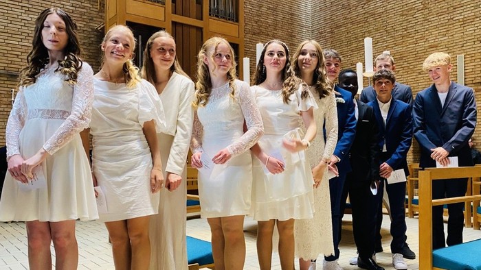 En gruppe unge piger i hvide tøjer og mænd i formelle klæder står sammen i en kirke.