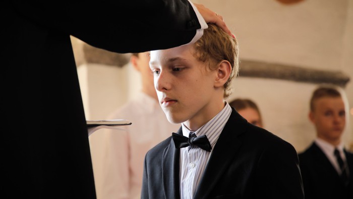 En ung dreng i mørk suite og hvid skjorte med bomme, der får sin hårbånd på.