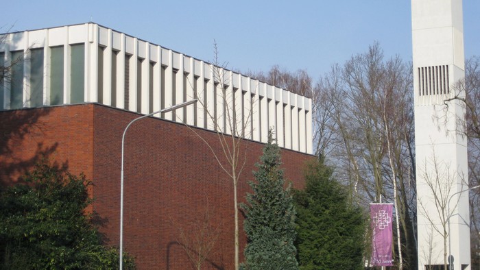 Modernes Gebäude mit weißer Fassade und hohem Turm neben Bäumen