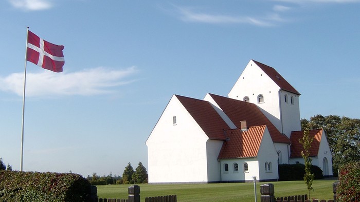 En hvid kirke med røde tag og en dansk flag på en stang foran