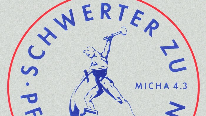 Das Logo zeigt eine Frau mit Hammer und Schwert, umgeben von Text in Blau und Rot