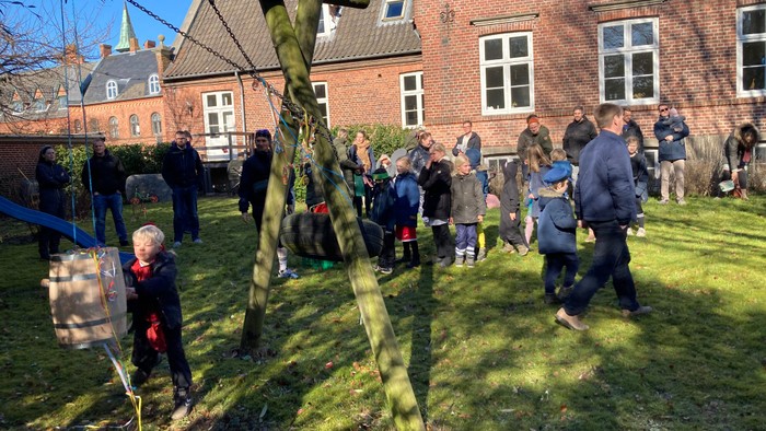 En gruppe af mennesker samles på en græsplæne foran et rødt teglstenhus, hvor en person tager et billede af en stor, grøn skørtelstand.