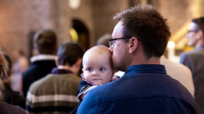 En mand holder et barn i en folkelig omgivelse.