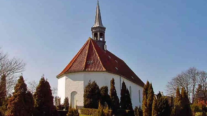 En hvid kirke med rødt tag og spir med kryds i en parkagtig omgivelse