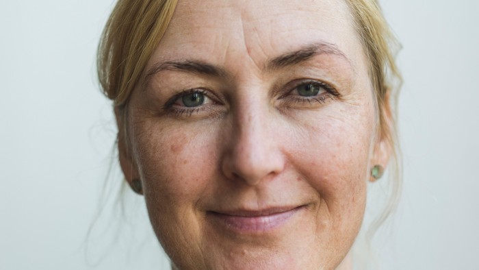 En kvinde med blondt hår og en mørk trøje med blomster.