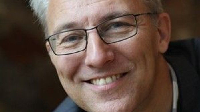 En smilende, eldre mand med briller og grå hår.