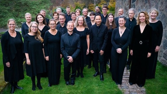 En gruppe af korister i sort tøj står sammen på en græsplæne