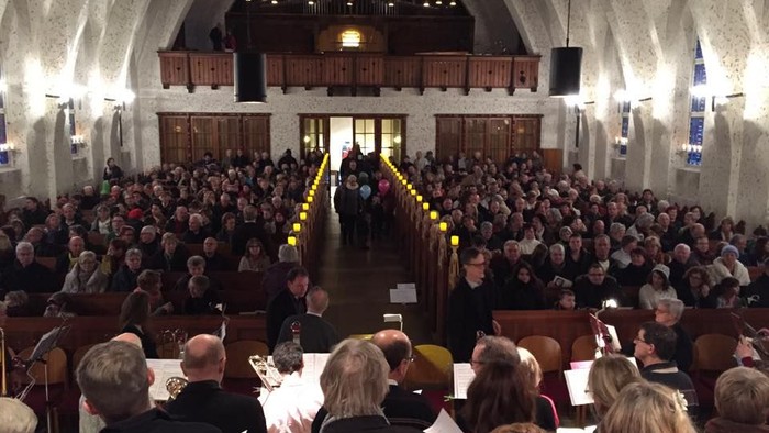 Große Menschenmenge in einer Kirche, viele sitzen, einige stehen, viele Kerzen brennen