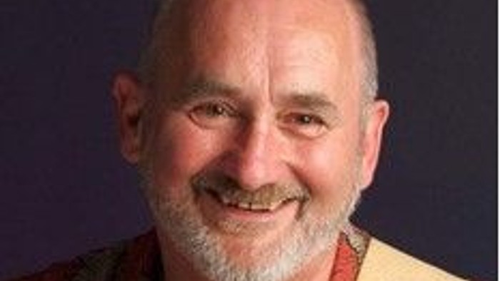 Ein glatzköpfiger Mann mit Bart lächelt in die Kamera.