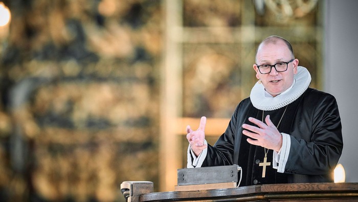 En præst står ved en pulpet og taler i en kirke.