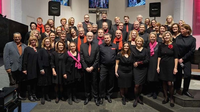 Ein großer Chor posiert für ein Gruppenfoto auf einer Bühne