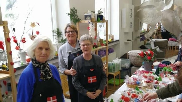Tre kvinder står ved en lang bord med juledekorationsgenstande