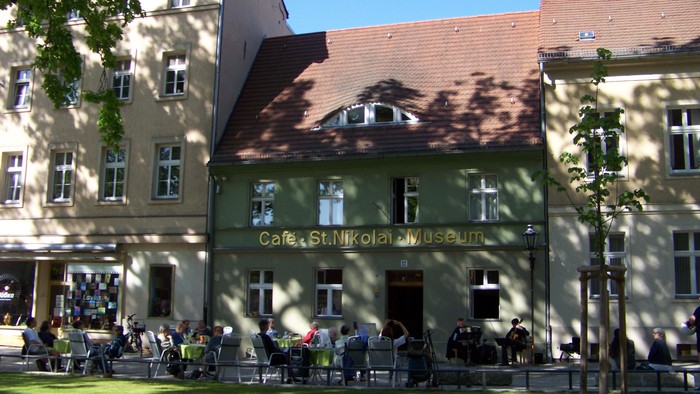 Das Bild zeigt ein Café mit Außenbestuhlung vor einem Gebäude.
