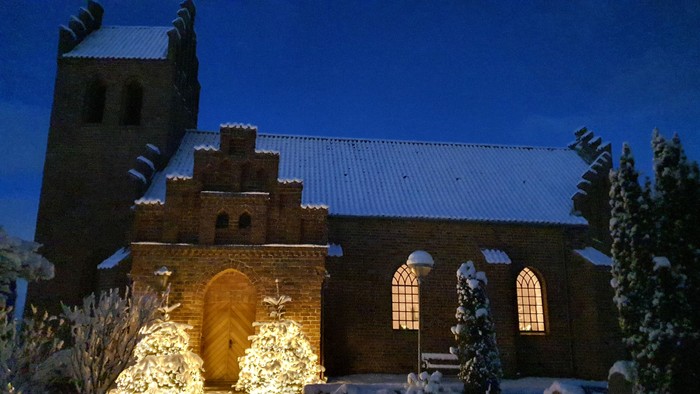 En middelalderlig kirke belyset ved natten med sne på træerne