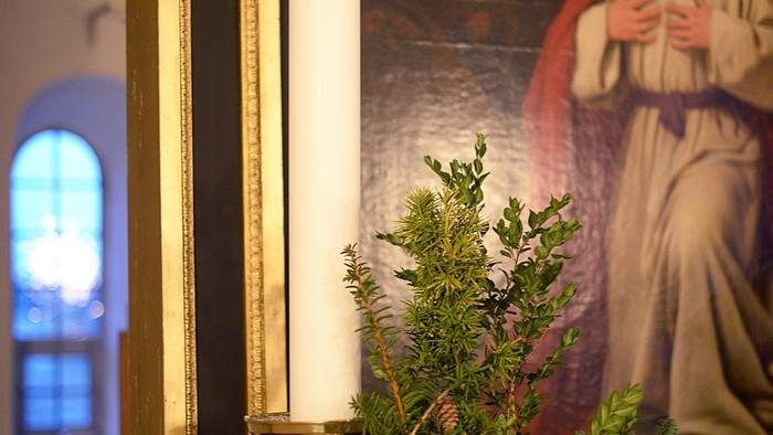 En lysende stearinlys og en grønne planter foran et bilde af Jesus