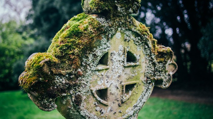 Ancient moss-covered stone cross in a lush green garden.