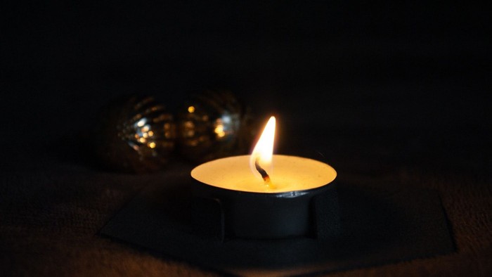 A lit candle in a dark room with shiny ornaments nearby.