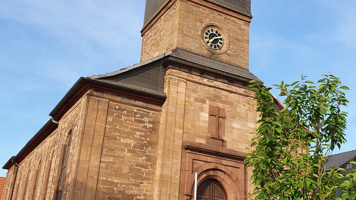 Das Bild zeigt eine alte Kirche mit einem Uhrturm und einem Vordach.