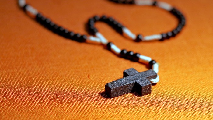 Ein Holzkreuz-Anhänger liegt auf einem orangefarbenen Stoff.