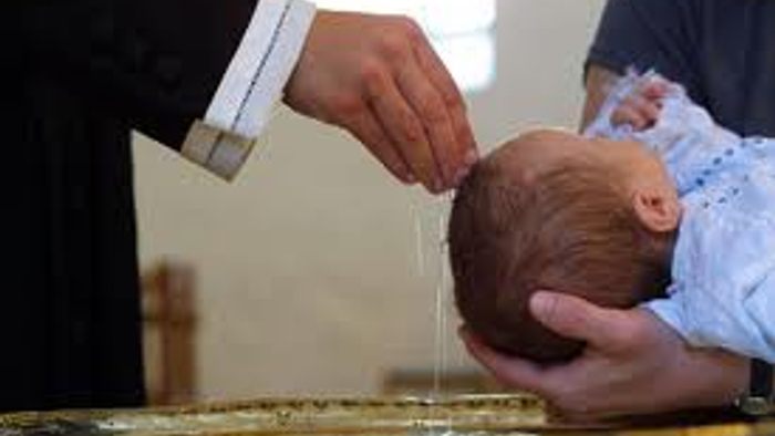 En person holdes et barns hoved, mens en anden person giver det mad.