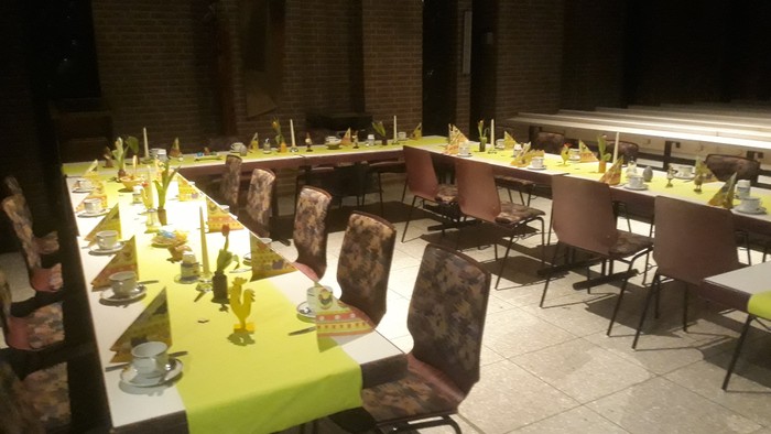 Ein festlich gedeckter Tisch mit gelben Tischdecken und Kerzen in einem großen Raum