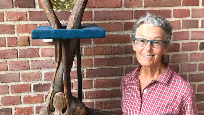 Kvinde står ved træskulptur og mur af røde teglsten