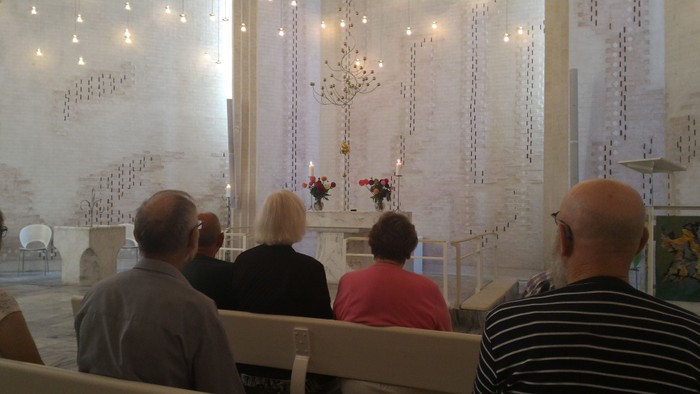 En gruppe mennesker sidder i en kirke og ser mod alteret.