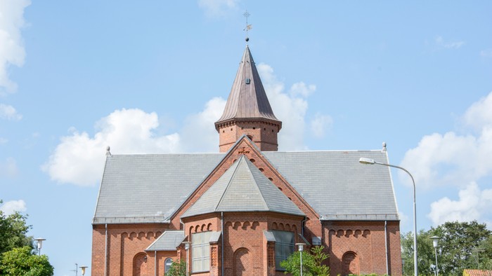 En rød murstenskirke med spiret og tårn i forgrunden