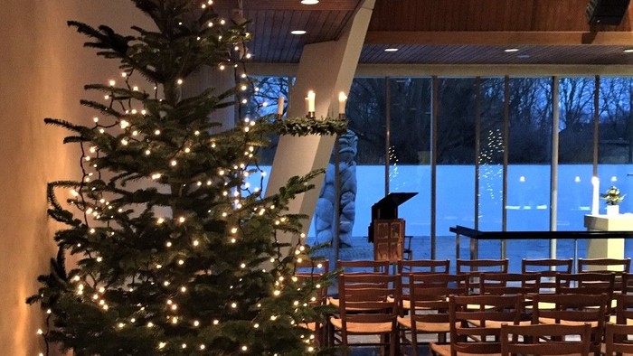 En juletree med lys og pynt i et rum med bord og stoler