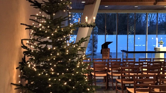 En juletree med lys og pynt i et rum med bord og stoler