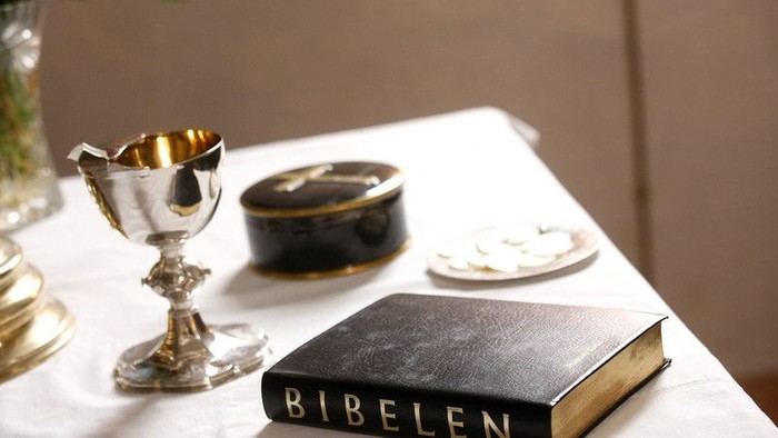 En hvid beklædning med en bibel, en gylden kelch og en sort og gylden skattekiste