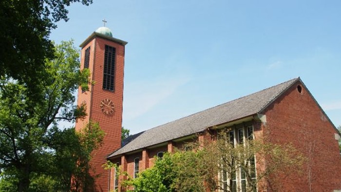 Kirchengebäude aus rotem Backstein mit hohem Turm und Uhr.