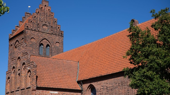Røde teglkirke med spids tårn og blå himmel.