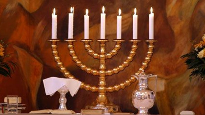 En gylden Menora med ni lys, placeret på en bord med blomster og vaser