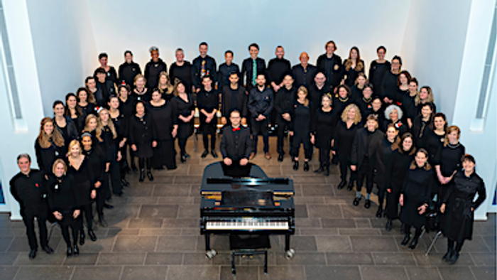 Ein großer Chor posiert vor einem Klavier in einem Raum