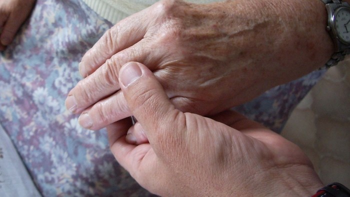 Zwei Hände, eine jüngere, eine ältere, halten einander.