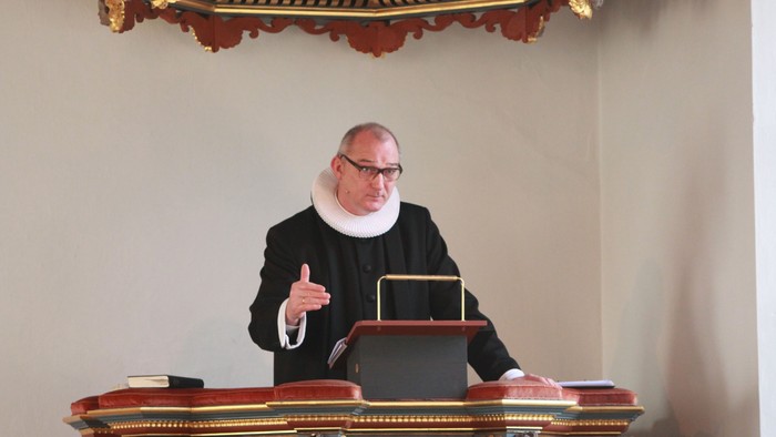 En præst i svart drømmer til et bord med boger.