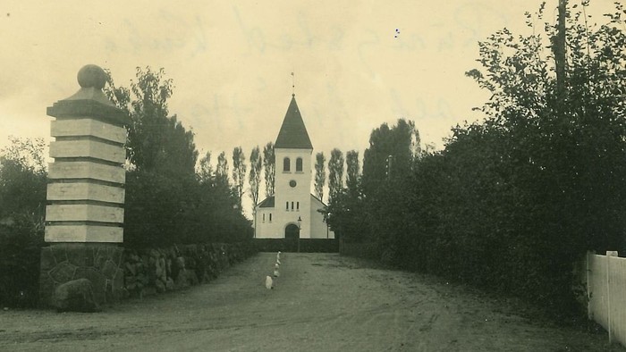 En gammel kirke med tårn og en klokketårn i en træket skov.