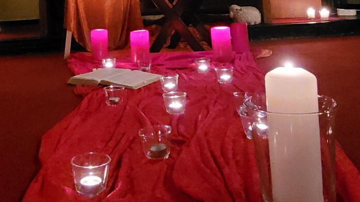 Ein Tisch mit roten Tischdecken und Kerzen, davor ein Kruzifix und ein Bild auf einem Altar