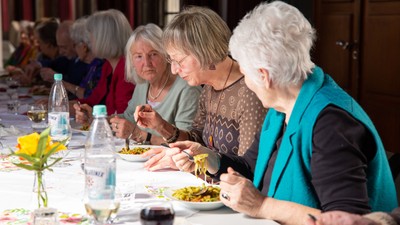 Eine Gruppe älterer Frauen sitzt bei einem gemeinsamen Essen an einem Tisch.
