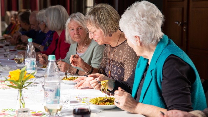 Eine Gruppe älterer Frauen sitzt bei einem gemeinsamen Essen an einem Tisch.